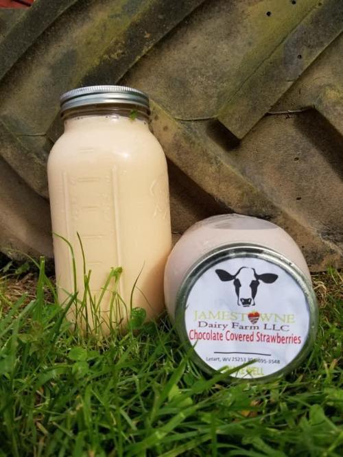 Two jars of dairy products on grass: a tall jar of cream and a round jar labeled "Chocolate Covered Strawberries."