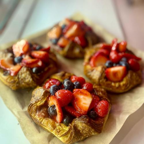 A close-up of pastry topped with fresh strawberries and blueberries on a parchment paper background.