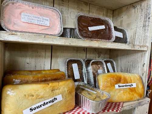 A wooden shelf displaying various baked goods, including sourdough loaves and labeled containers of different breads.