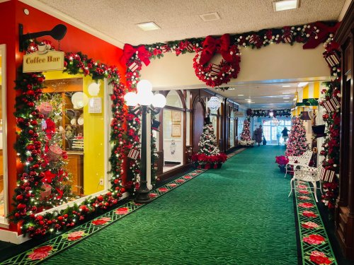 Festively decorated indoor corridor with Christmas trees, wreaths, and a coffee bar, featuring vibrant red and green decor.