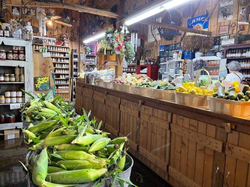 A rustic market interior with baskets of fresh produce, including corn, and shelves stocked with jars and goods.