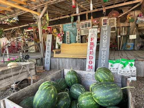 A rustic market scene with watermelons in a wooden crate and decorative signs reading "Blessed," "Freedom," and "Home."