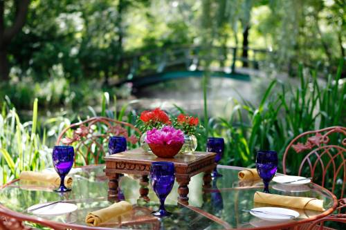 A beautifully set outdoor table with purple glasses, yellow napkins, and vibrant flowers, surrounded by lush greenery.