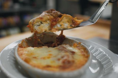 A fork lifting a cheesy, baked lasagna from a white dish, showcasing layers of pasta and sauce.