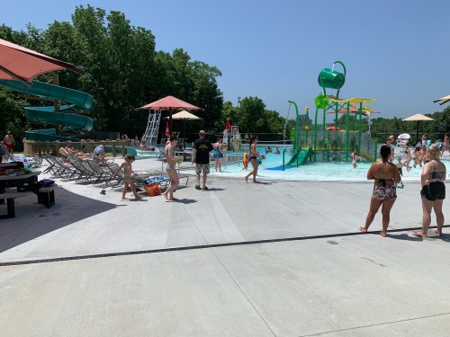 A busy outdoor water park with slides, a splash area, and people enjoying the sun and water activities.