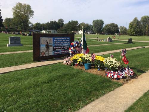 A memorial site with flowers, flags, and a sign honoring veterans in a peaceful cemetery setting.