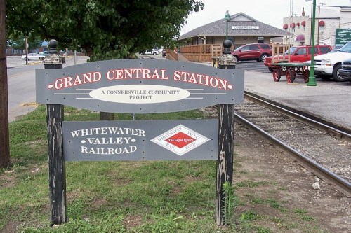Sign for Grand Central Station, a community project, near the Whitewater Valley Railroad, with a train track in the background.