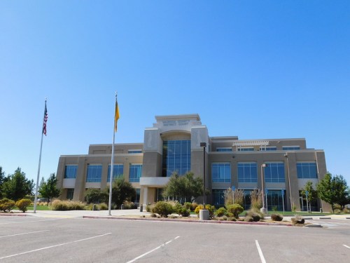 Modern courthouse building with large glass entrance, surrounded by greenery and clear blue sky. Flags are displayed in front.