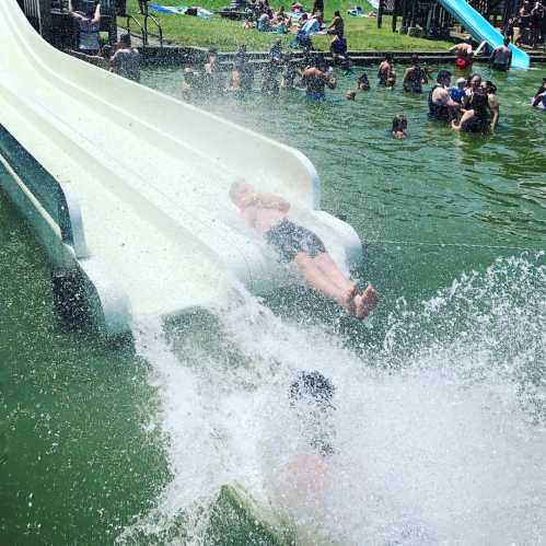 A water slide at a pool with people splashing and enjoying a sunny day.