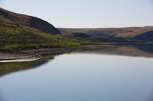 A calm lake reflects the surrounding hills and clear sky, with a shoreline lined by greenery.