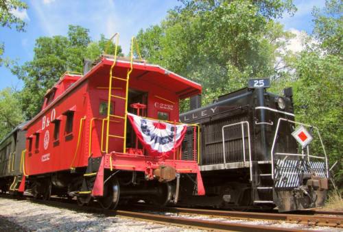 A red caboose and a black locomotive parked on a railway surrounded by lush greenery.
