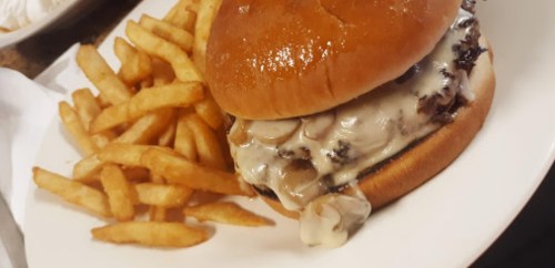 A juicy burger with melted cheese and mushrooms, served with a side of golden French fries on a white plate.