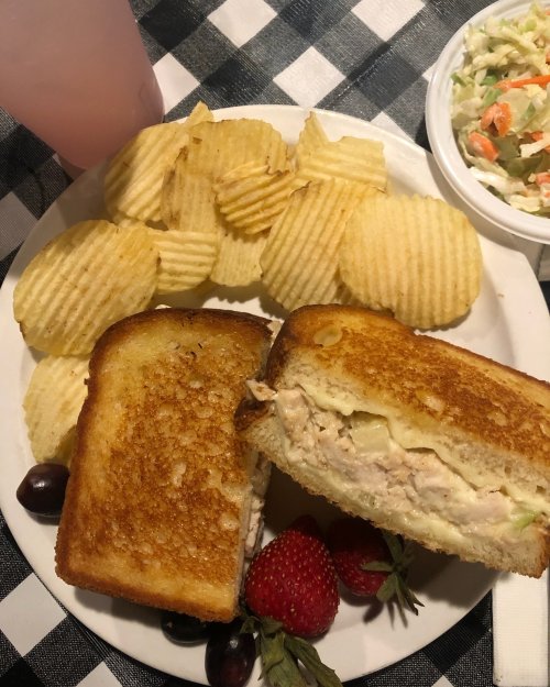 A plate with a grilled sandwich, potato chips, strawberries, and coleslaw on a checkered tablecloth.