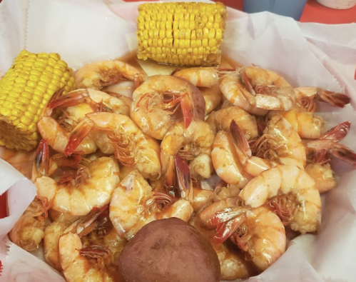 A basket of shrimp with corn on the cob and a small roll, all coated in a flavorful sauce.