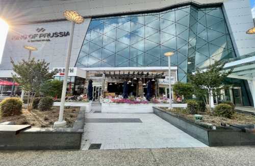 Exterior view of the King of Prussia Mall entrance, featuring modern architecture and landscaped flower beds.