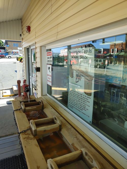 A mining sluice for fossil hunting, displayed outside a shop with informational signs and a view of the street.