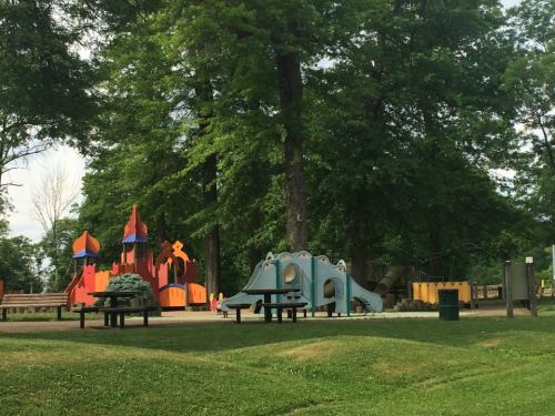 Colorful playground equipment surrounded by trees in a park, featuring slides and climbing structures.