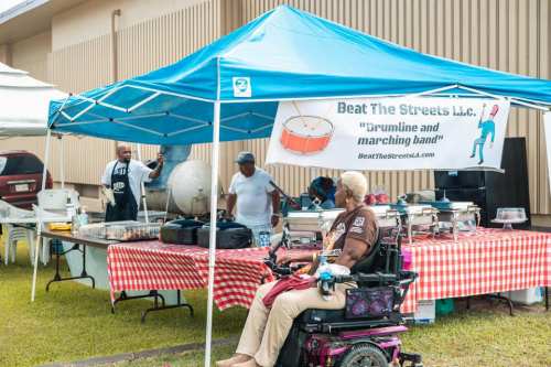 A food booth under a blue tent with a banner for "Beat The Streets" and people serving food at a community event.