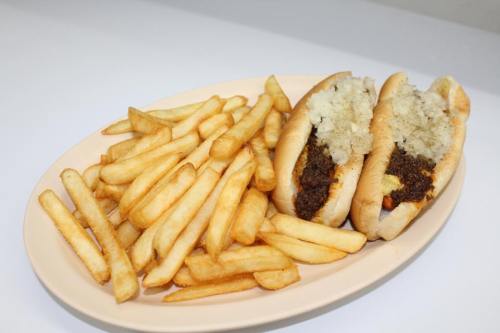 Two chili dogs topped with onions on a plate, accompanied by a generous serving of golden French fries.