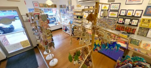 A colorful store interior filled with art prints, toys, and crafts, featuring displays and a welcoming entrance.