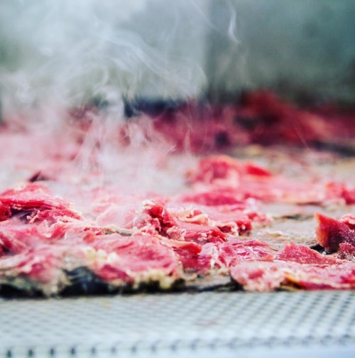 Thin slices of raw meat on a grill, with steam rising in the background.
