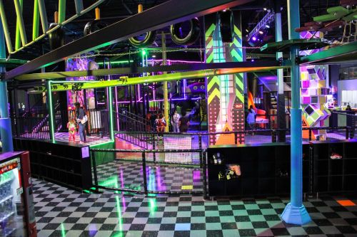 A vibrant indoor play area with colorful lights, climbing structures, and a checkered floor.