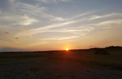 A serene sunset over a grassy landscape, with soft clouds illuminated by warm orange and yellow hues.
