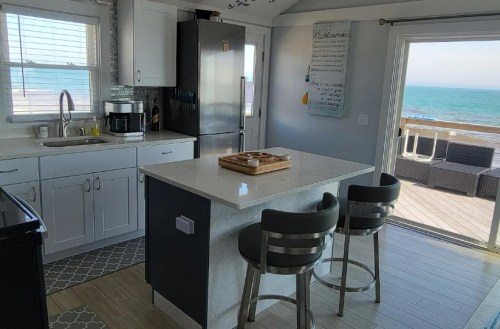 Bright kitchen with modern appliances, a central island, and a view of the ocean through large windows.