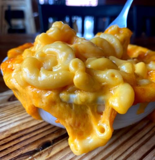 A close-up of creamy macaroni and cheese in a white bowl, with a fork lifting a portion.