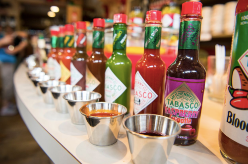 A row of various Tabasco sauce bottles and small metal cups filled with different sauces on a counter.
