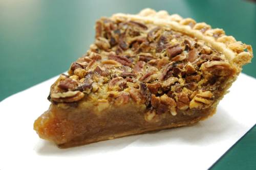 A slice of pecan pie on a white napkin, featuring a golden crust and a rich, nutty filling.