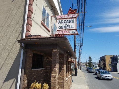 Sign for Arcaro & Genell restaurant, with a clear blue sky and street view in the background.