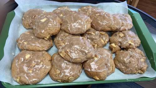 A tray of freshly baked cookies topped with a glossy brown glaze, featuring chunks of apple throughout.