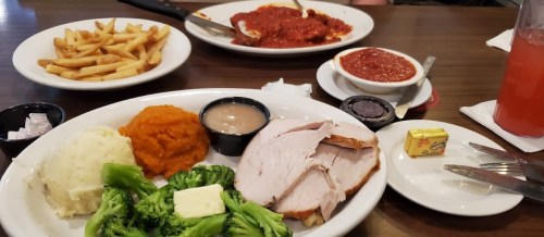 A plate with turkey, mashed potatoes, sweet potatoes, broccoli, and butter, alongside fries and a pasta dish.