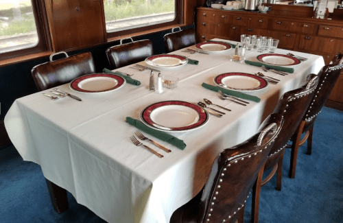 A dining table set with plates, utensils, and glasses, surrounded by wooden chairs in a cozy interior.