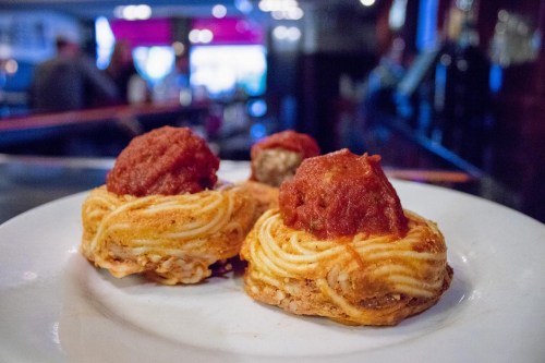 A plate of spaghetti nests topped with meatballs and marinara sauce, set in a dimly lit restaurant.
