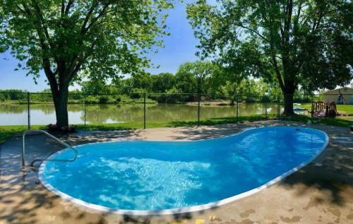 A serene outdoor pool surrounded by trees, with a view of a calm lake in the background on a sunny day.
