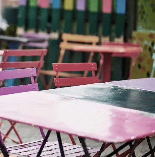 Colorful outdoor tables and chairs in a vibrant setting, featuring pink and black surfaces.