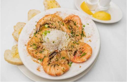 A plate of shrimp with rice, garnished with herbs, served with slices of bread and lemon wedges on the side.