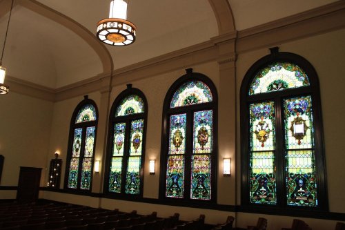 Stained glass windows in a church, featuring intricate designs and vibrant colors, illuminate the interior space.