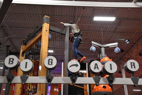 A person climbs a vertical structure at an indoor adventure park, with "BIG AIR" signage visible below.