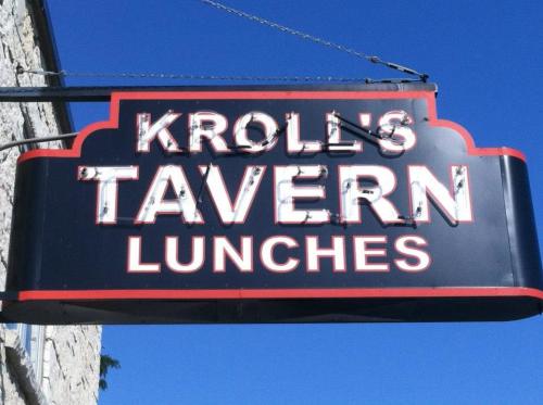 Sign for Kroll's Tavern, featuring the words "TAVERN" and "LUNCHES" in bold letters against a blue sky.