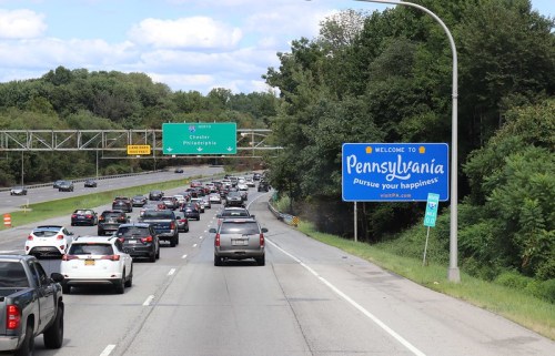 Traffic on a highway with a "Welcome to Pennsylvania" sign and green directional signs in the background.