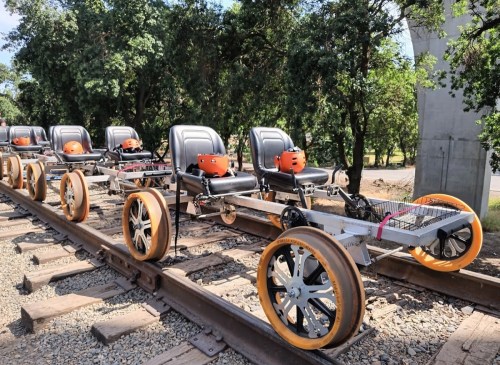 A row of pedal-powered rail carts on a railway track, surrounded by greenery.