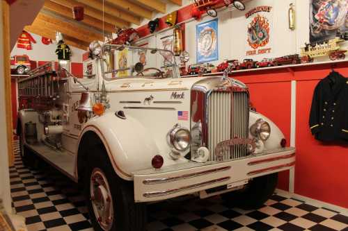 A vintage white fire truck displayed in a museum with red walls and various fire-related memorabilia.