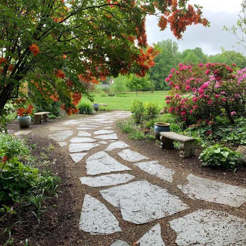 A stone pathway winds through a lush garden with vibrant flowers and greenery under a cloudy sky.