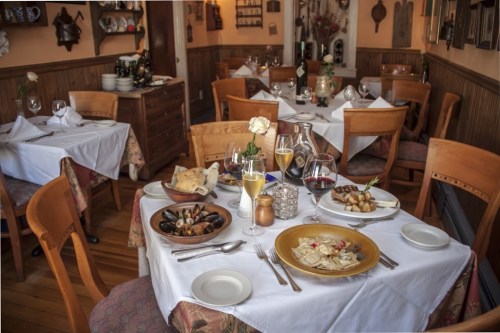 A cozy restaurant table set with elegant dishes, wine glasses, and a flower centerpiece, creating a warm dining atmosphere.