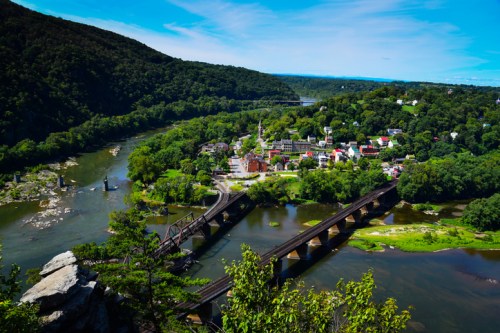 Aerial view of a river winding through green hills, with a small town and a bridge visible in the foreground.