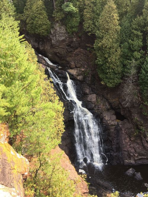 A scenic waterfall cascading down rocky cliffs, surrounded by lush green trees.