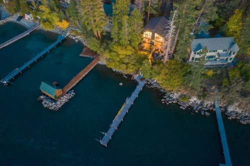Aerial view of a serene lake with wooden docks and cozy homes surrounded by trees at sunset.